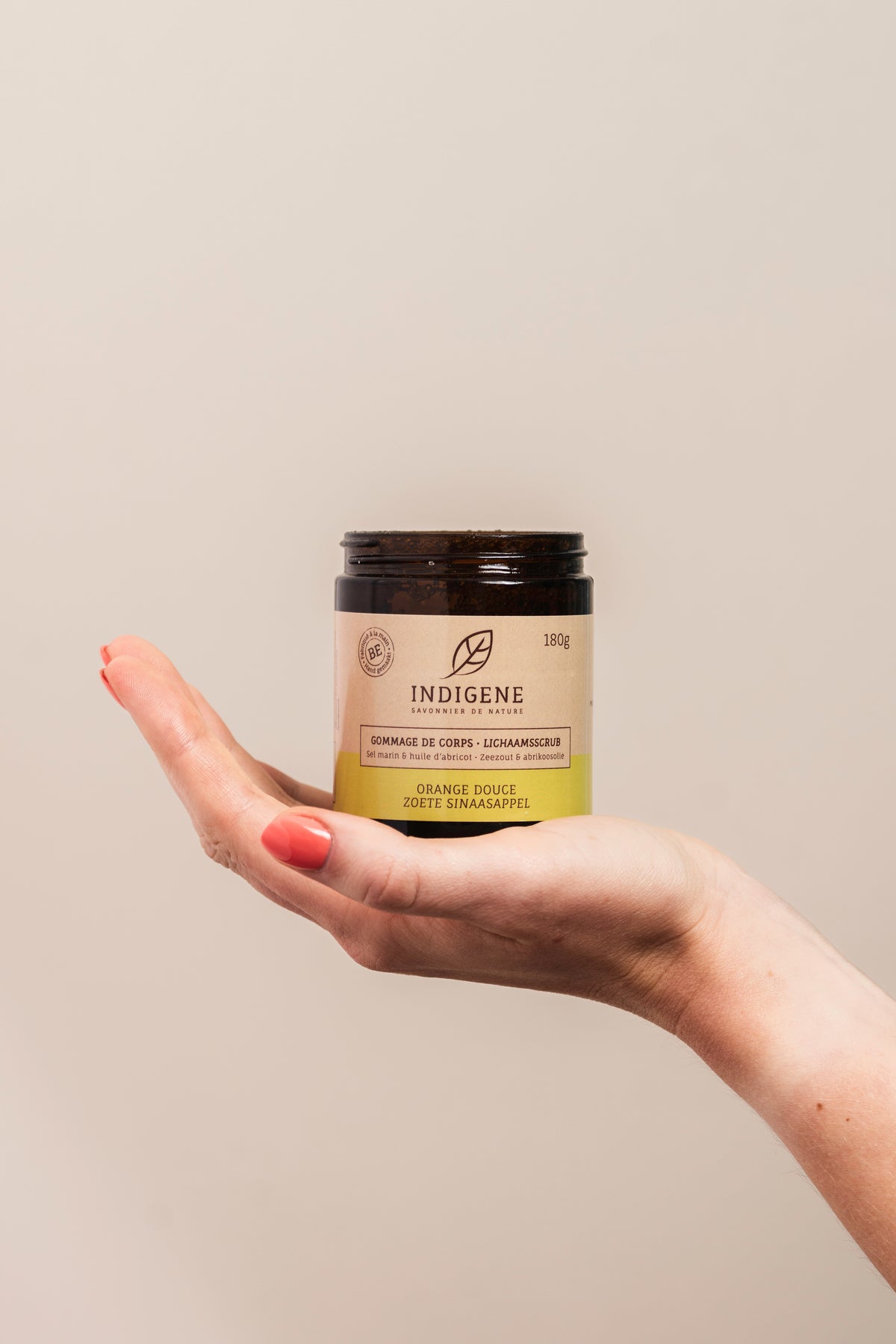Pot de gommage pour le corps naturel Indigene au parfum d'orange douce, présenté au creux de la main