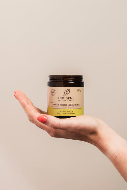 Pot de gommage pour le corps naturel Indigene au parfum d'orange douce, présenté au creux de la main