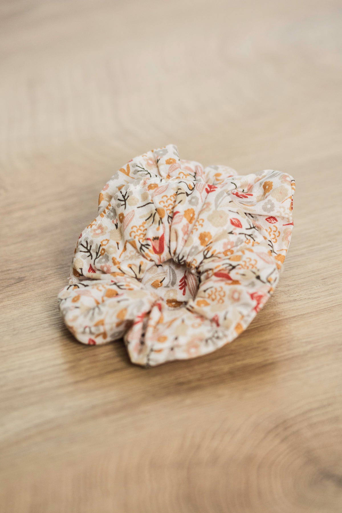 Chouchou à cheveux en tissu imprimé de motifs floraux et champêtres posé sur du bois