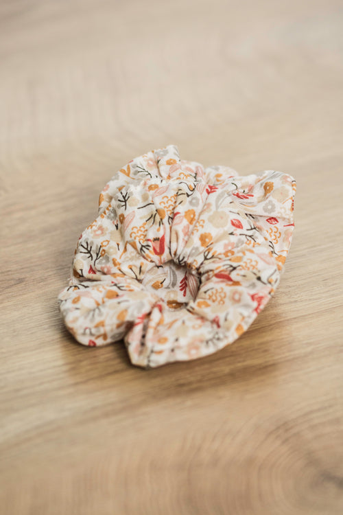 Chouchou à cheveux en tissu imprimé de motifs floraux et champêtres posé sur du bois