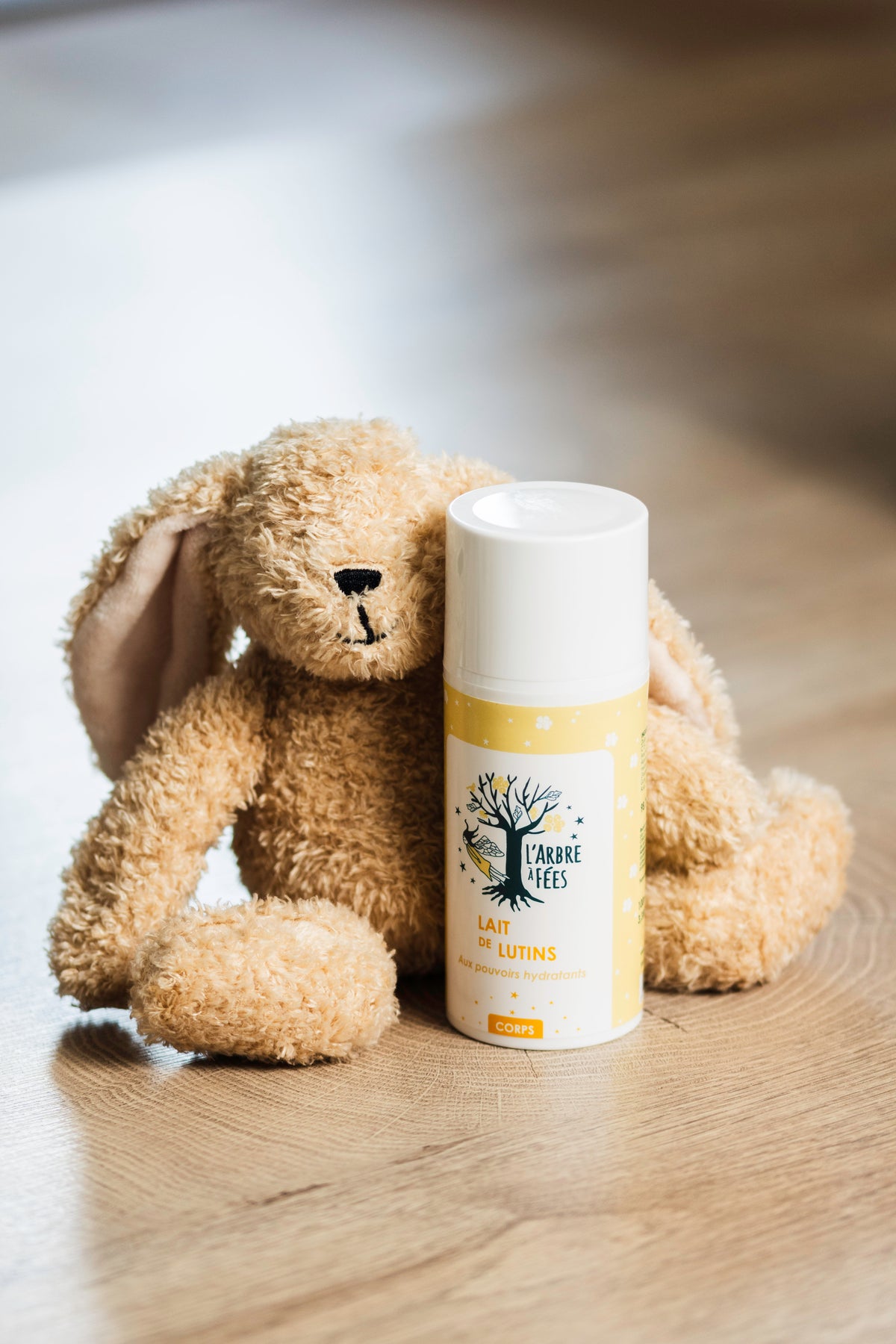 Flacon de lait de lutins hydratant pour le corps L'Arbre à Fées posé à côté d'un doudou lapin