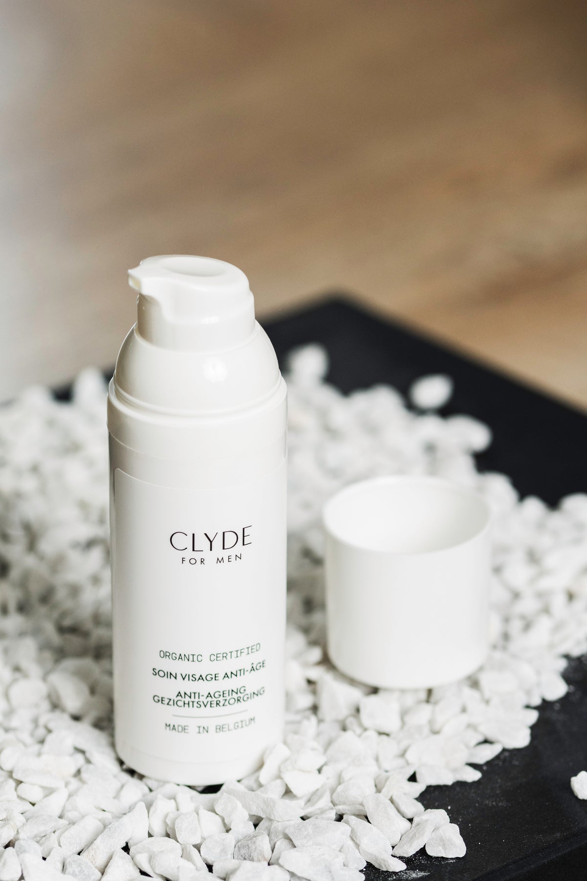 Flacon de soin visage anti-âge certifié bio Clyde for Men sur fond de petits cailloux blancs.